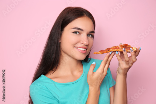 Young woman eating slice of delicious pizza on color background