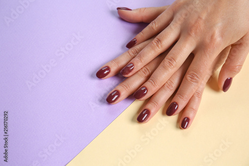 Hands of woman with stylish dark red manicure on color background