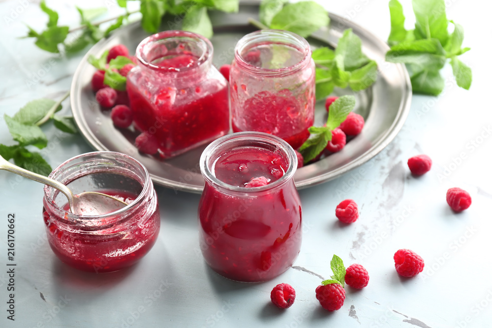 Glass jars with tasty raspberry jam on light table Glass jars with tasty raspberry jam on light table