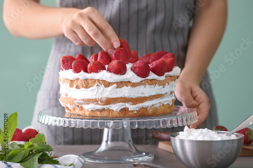 Woman decorating cake with strawberries, closeup