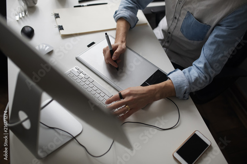 Foto Young male designer using graphics tablet while working with com