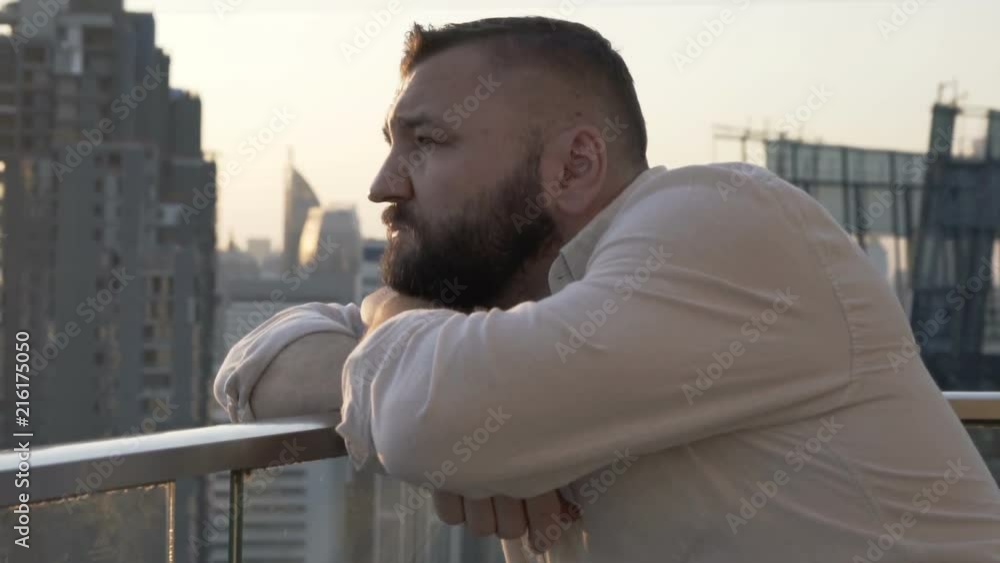 Pensive man leaning on the balcony and admires the city during sunset
Pensive man leaning on the balcony and admires the city during sunset