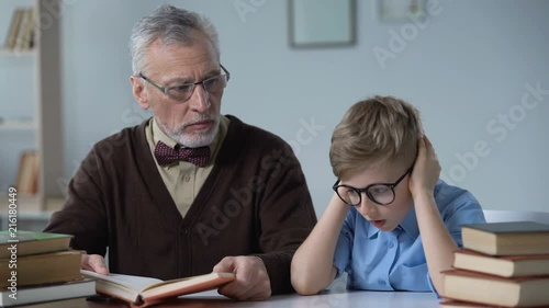 Grandfather reading aloud book, little boy looks bored, generation gap problem