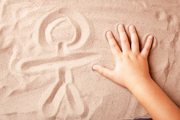 Child is drawing finger on the sand symbol of person