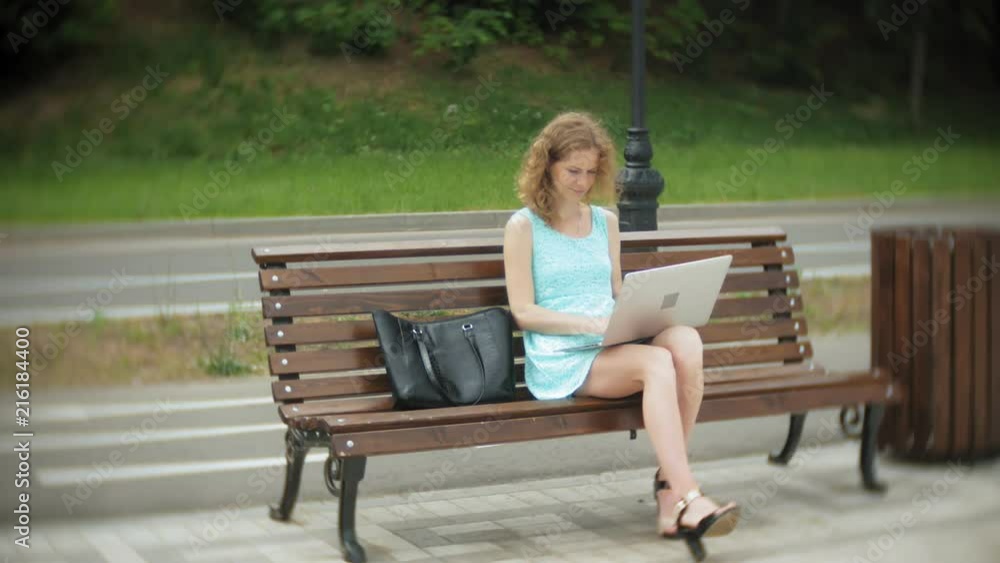 A woman sitting on a bench on the beach using a laptop A woman sitting on a bench on the beach using a laptop