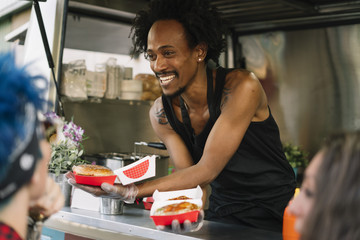 Smiling food vendor hands food to waiting customer