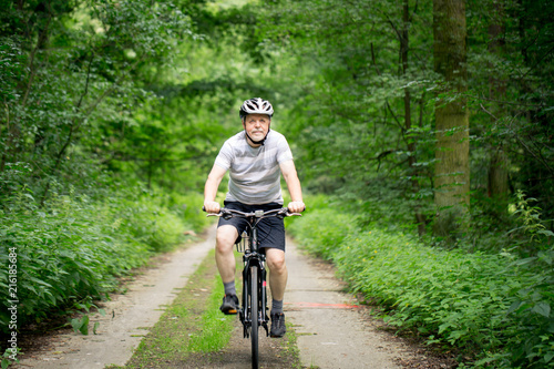 Senior man on a bike during lovely summer time in forest, smiling, enjoying trip
