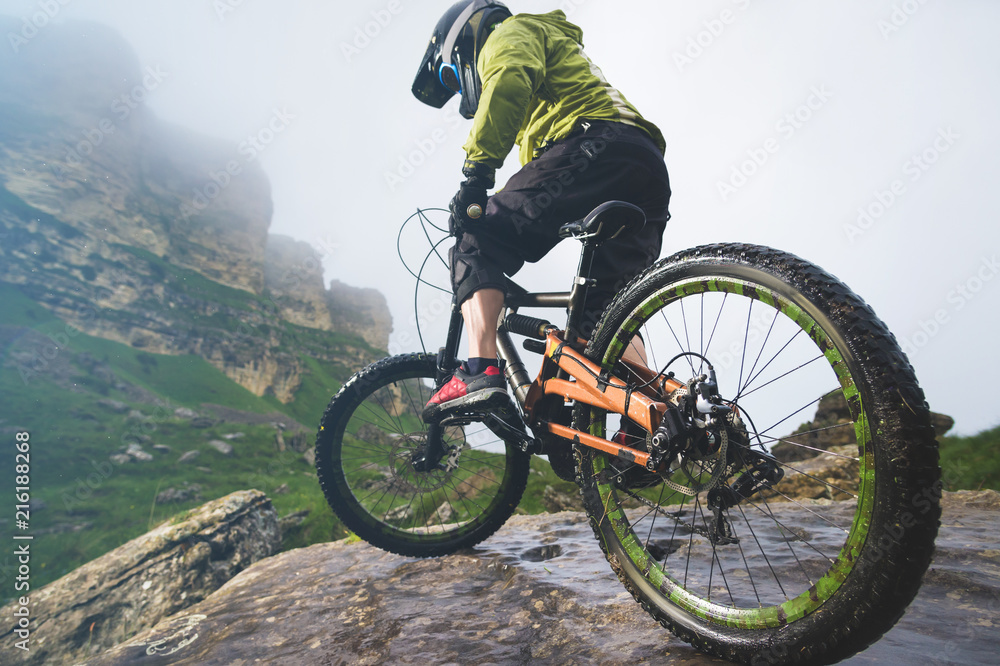 Legs of bicyclist and rear wheel close-up view of back mtb bike in mountains against background of rocks in foggy weather. The concept of extreme sports Legs of bicyclist and rear wheel close-up view of back mtb bike in mountains against background of rocks in foggy weather. The concept of extreme sports