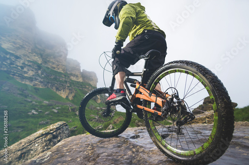 Fototapeta Naklejka Na Ścianę i Meble -  Legs of bicyclist and rear wheel close-up view of back mtb bike in mountains against background of rocks in foggy weather. The concept of extreme sports