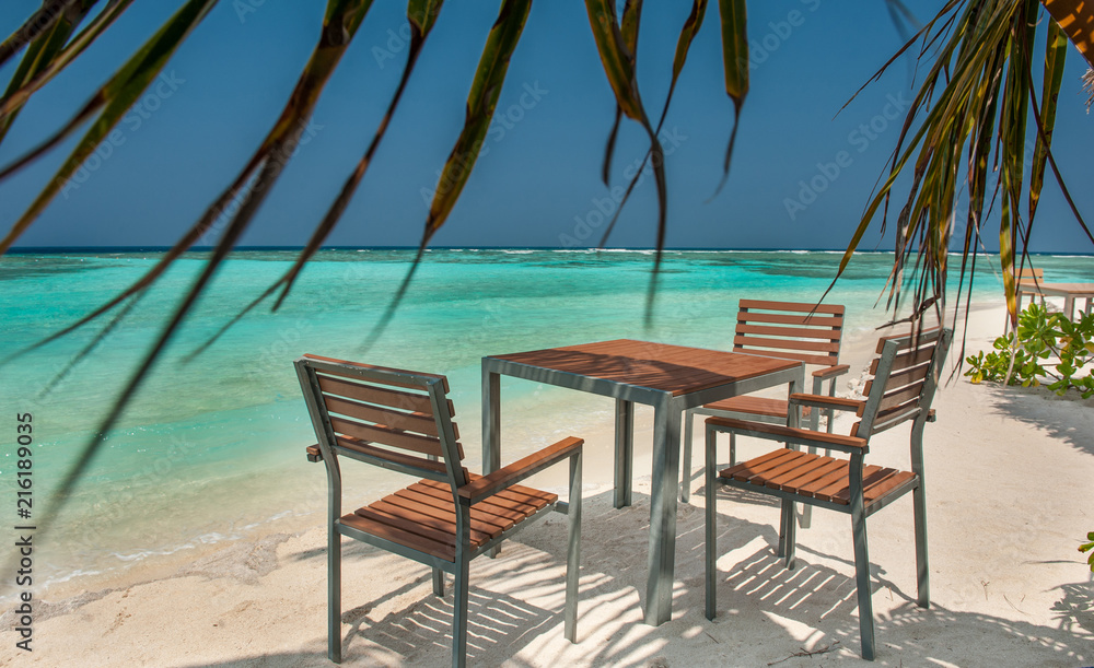 table and chairs on the ocean beach on a tropical island in the Maldives.Tables and chairs in the shadow of palm tree on a tropical island.
