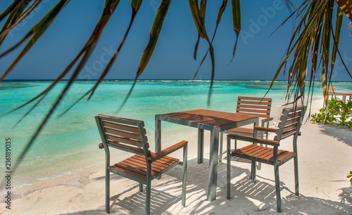 Fototapeta Naklejka Na Ścianę i Meble -  table and chairs on the ocean beach on a tropical island in the Maldives.Tables and chairs in the shadow of palm tree on a tropical island.