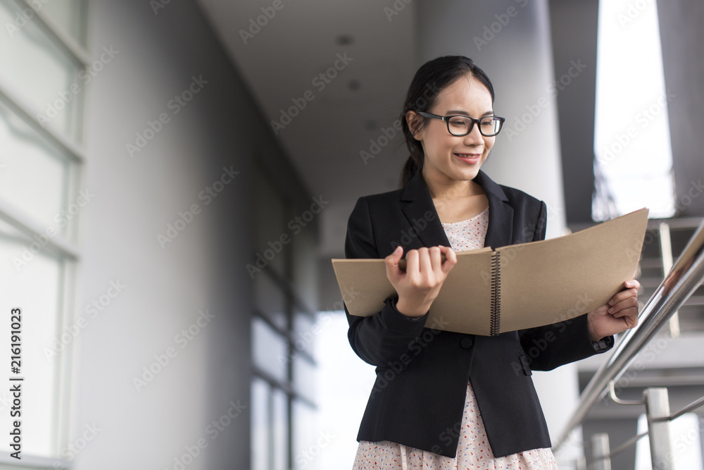 Young Asian business woman wear suit holding file document, standing at office Young Asian business woman wear suit holding file document, standing at office