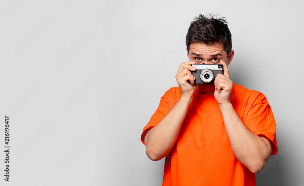 Young handsome man in orange t-shirt with vintage camera. Studio image on white background Young handsome man in orange t-shirt with vintage camera. Studio image on white background