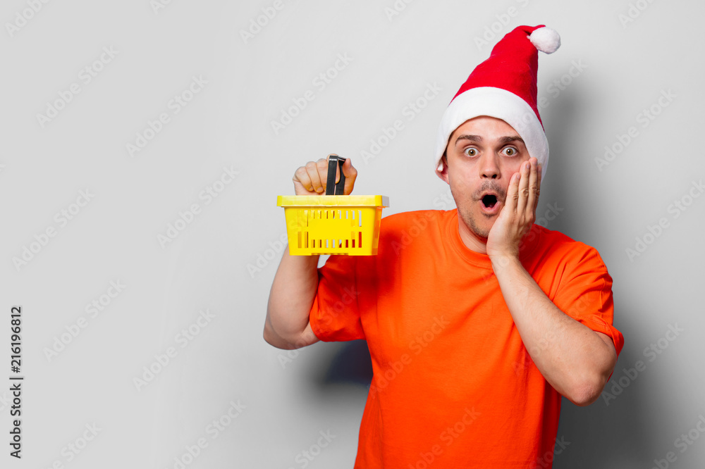 Young handsome man in orange t-shirt with Christmas hat and supermarket basket. Studio image on white background Young handsome man in orange t-shirt with Christmas hat and supermarket basket. Studio image on white background