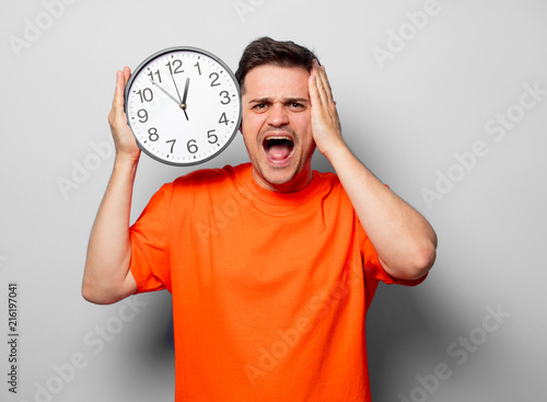 Young handsome man in orange t-shirt with big clock. Studio image on white background