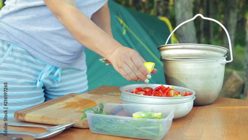 A young woman squeezes lemon juice into a bowl with a salad on a picnic A young woman squeezes lemon juice into a bowl with a salad on a picnic