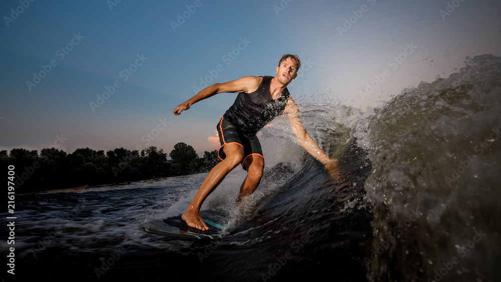 Fototapeta premium Active strong young man riding down the river waves in evening