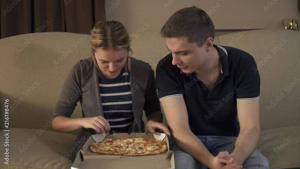 Young couple with a box of pizza sits on the couch Young couple with a box of pizza sits on the couch