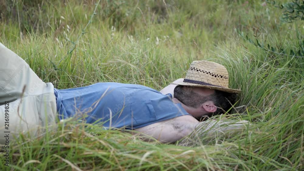 Attractive, fit young man relaxing lying in a grass field, wearing straw hat Attractive, fit young man relaxing lying in a grass field, wearing straw hat