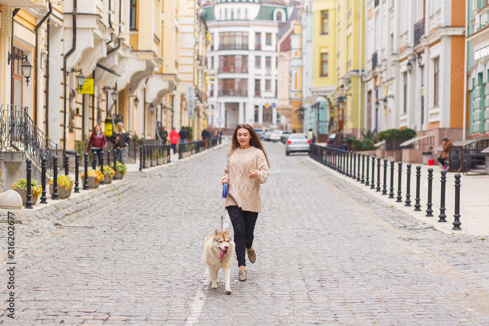 The woman take a walk with husky dog at sunny autumn day on old European city street. Horizontal view