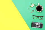 Top view of a cup of coffee, a branch of a white rose, gold rings, glasses and a vintage camera with a place for text on a bright yellow-green graph paper background. Woman background. flat lay