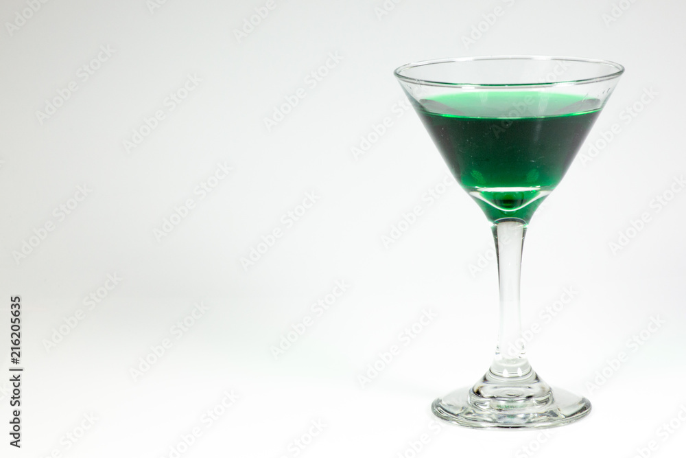 Halloween inspired green color cocktail in a clear glass sitting on a white table waiting to be enjoyed. Halloween inspired green color cocktail in a clear glass sitting on a white table waiting to be enjoyed.