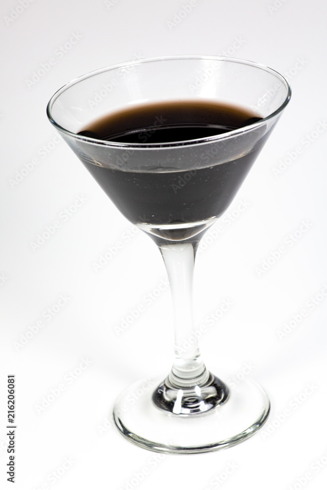 Halloween inspired black color cocktail in a clear glass sitting on a white table waiting to be enjoyed. Halloween inspired black color cocktail in a clear glass sitting on a white table waiting to be enjoyed.