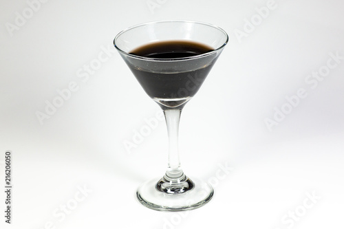 Halloween inspired black color cocktail in a clear glass sitting on a white table waiting to be enjoyed.