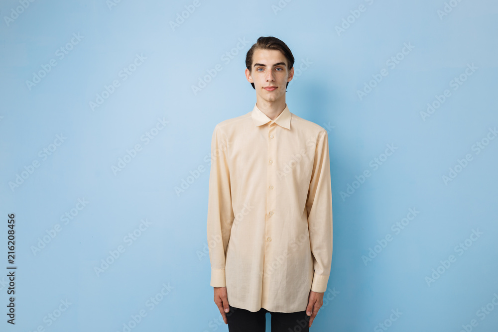 Fototapeta premium Handsome young thin dark-haired guy with blue eyes wearing yellow shirt posing over blue wall