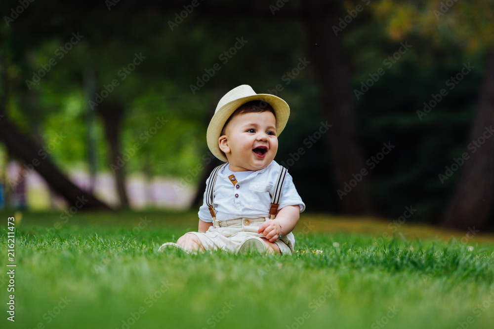 Funny and chubby baby sitting on the grass dressed in a vintage look of hat and suspenders, enjoying a spring day in the park Funny and chubby baby sitting on the grass dressed in a vintage look of hat and suspenders, enjoying a spring day in the park