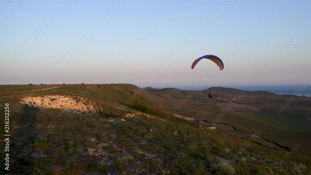 Close-up: paraglider is flying over the edge of the hill against the sea and the Sun Close-up: paraglider is flying over the edge of the hill against the sea and the Sun