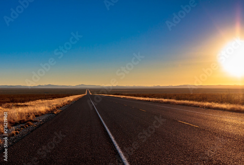 Open desert road leading to a mountain range at sunset