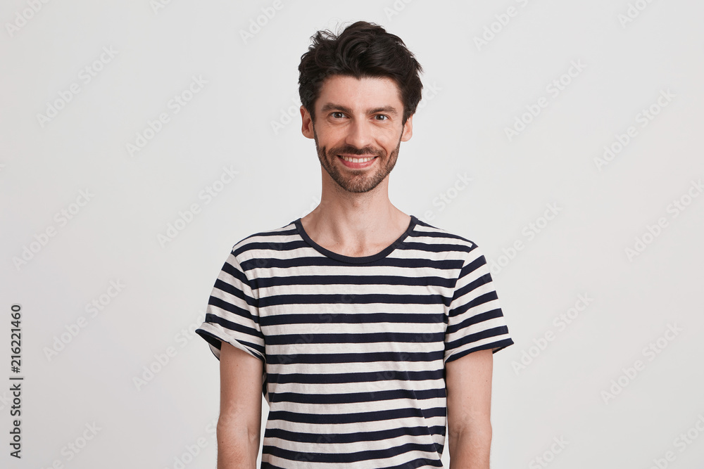 Obraz premium Closeup of cheerful handsome young man with bristle wears striped t shirt feels happy and looks directly in camera isolated over white background
