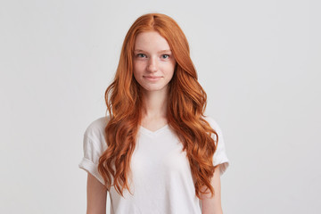 Closeup of happy attractive young woman with long wavy red hair and freckles wears stylish t shirt looks happy and smiling isolated over white background