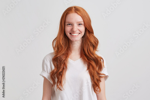 Closeup of happy pretty redhead young woman with long wavy hair and freckles wears stylish t shirt feels satisfied and looks confident isolated over white background