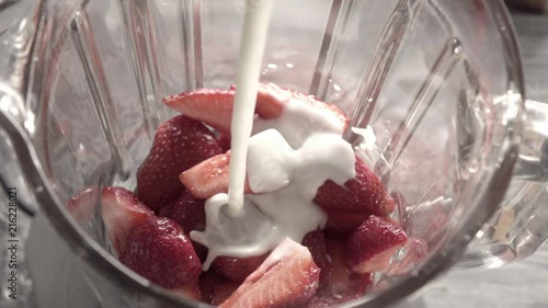 Milk cream with splash pouring into the glass jar of the blender with red, ripe strawberries fruit. Top view. Full HD video, 240fps,1080p.