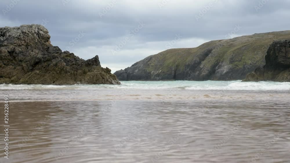 Low to ground wide shot on Sango sands in Durness, Scotland, water running back to see underneath camera. tide going out, rocks in front Low to ground wide shot on Sango sands in Durness, Scotland, water running back to see underneath camera. tide going out, rocks in front