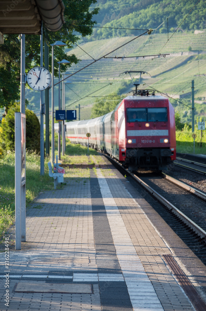 Red train entering train station with focus on platform clock