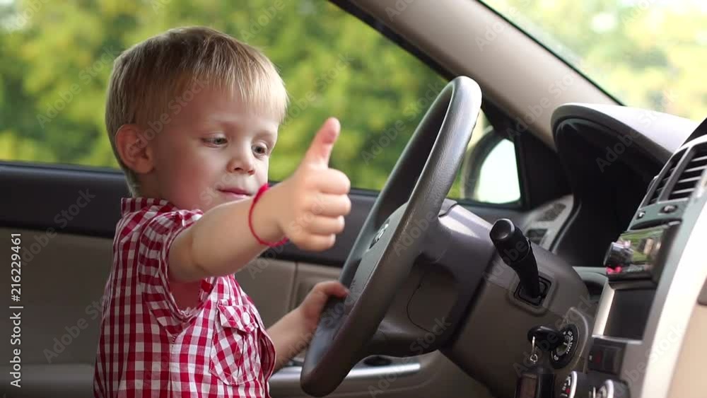 A little happy boy is sitting behind the wheel of a car and shows his thumb up. Car purchase. Portrait of a child in a new car driving, he shows his thumb up. A little happy boy is sitting behind the wheel of a car and shows his thumb up. Car purchase. Portrait of a child in a new car driving, he shows his thumb up.