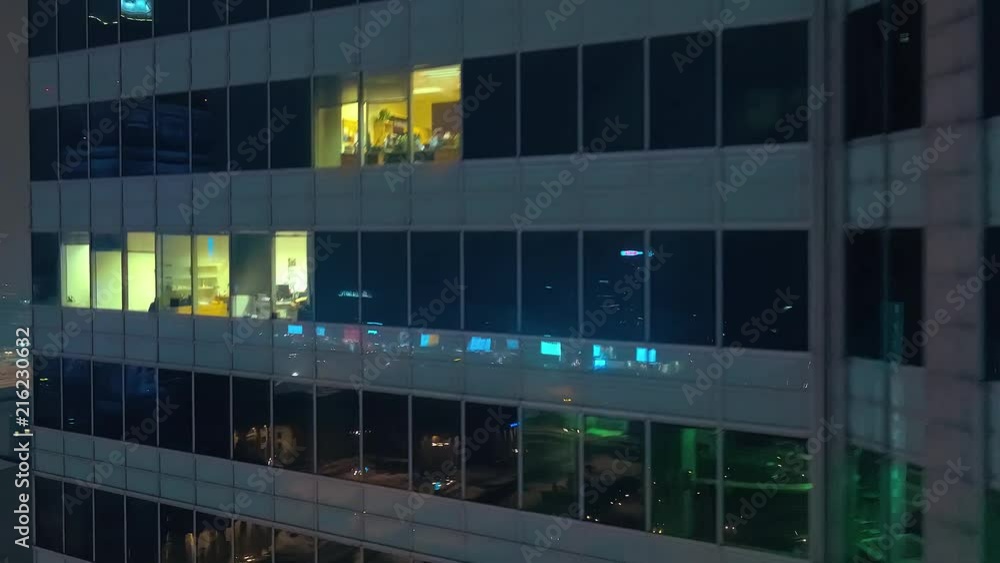 The drone is flying down a modern, glazed skyscraper in which the city center is reflected.