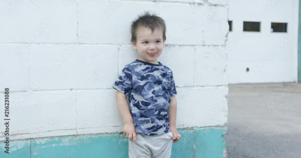 Toddler boy standing against white brick wall - counting with fingers Toddler boy standing against white brick wall - counting with fingers