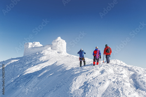 Three brave rescuers explore the terrain of snowy slope for avalanche danger against snow capped old observatory at peak of Carpathian mountain. Rear view. Winter seasonal landscape. Wanderlust series