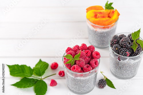 Food and drink, healthy eating and dieting concept. Homemade white chia pudding with fresh berries and green leaves for breakfast on a light kitchen table. Three glasses, raspberry, blackberry,apricot