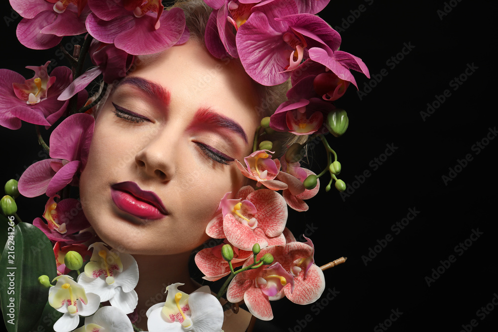 Young woman with dyed eyebrows surrounded by flowers on black background Young woman with dyed eyebrows surrounded by flowers on black background