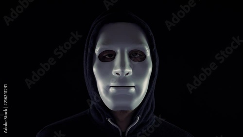 Video of a man in mask wearing a hoodie opening eyes and giving a creepy look at the looker in isolated dark background