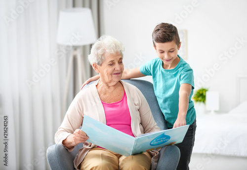 Senior nanny reading book to little boy indoors
