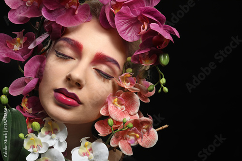 Fototapeta Naklejka Na Ścianę i Meble -  Young woman with dyed eyebrows surrounded by flowers on black background