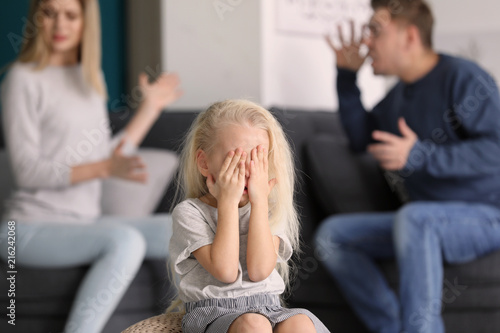 Sad little girl in room with quarreling parents. Family conflict