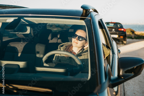 Portrait of a young smiling joyful woman or girl driver inside the car. Daily trips on transport or tourism, road travel or adventure.