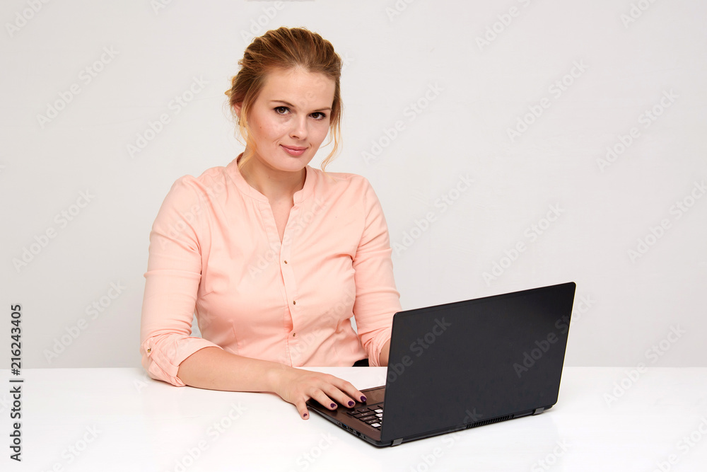 Portrait of a beautiful blond business girl on a white background sitting at the table with a laptop. Portrait of a beautiful blond business girl on a white background sitting at the table with a laptop.